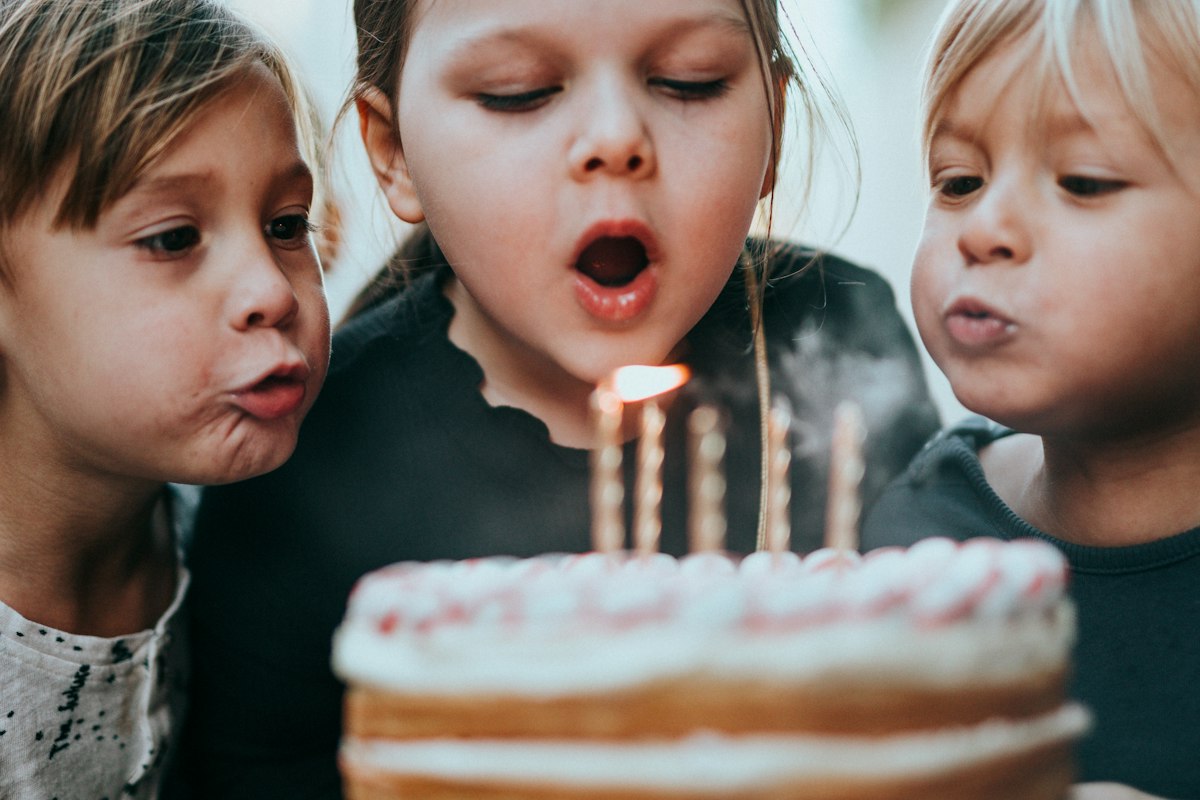 Three kids blowing out the candles on a birthday cake