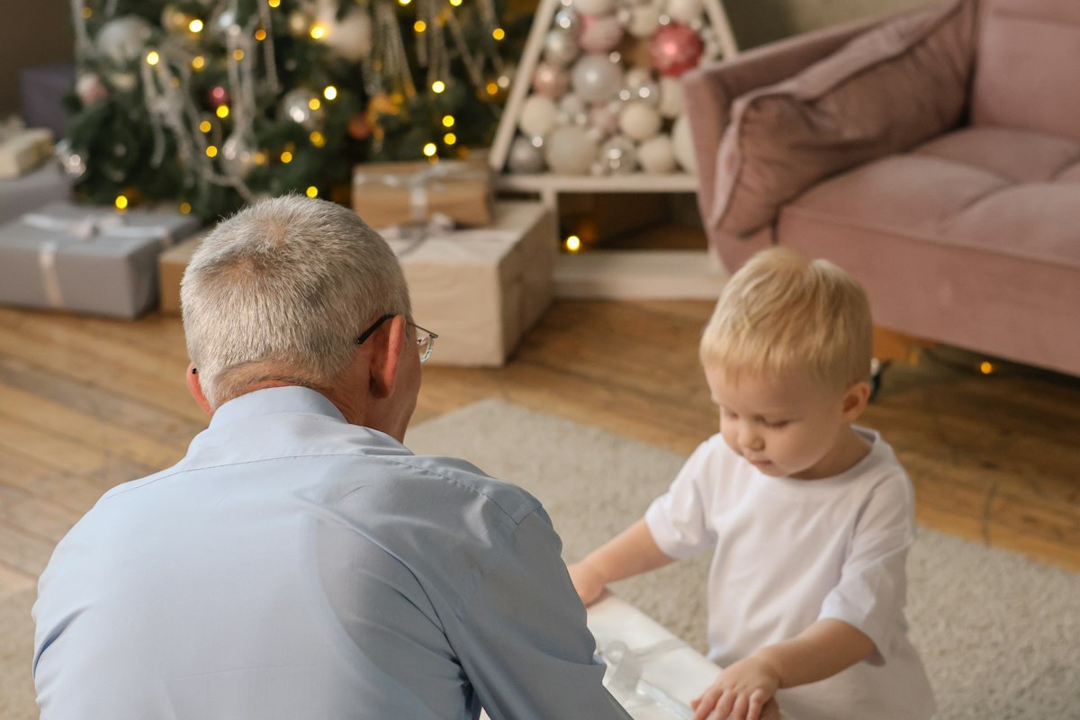 A grandfather and a small child opening a gift by the Christmas tree