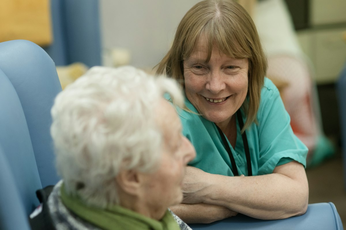 A smiling nurse in green scrubs leaning toward an elderly patient