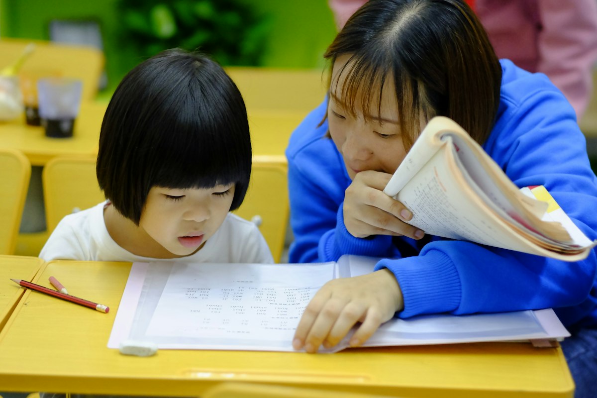 A teacher leaning in to help a young student with her writing